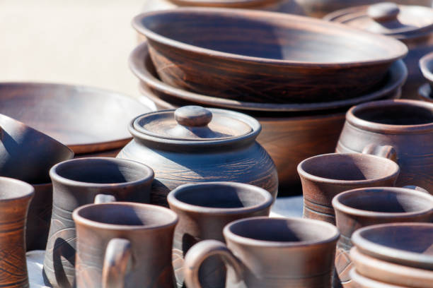 A table full of brown pottery, including bowls, cups, and a vase. The table is covered with a variety of shapes and sizes, creating a sense of abundance and variety