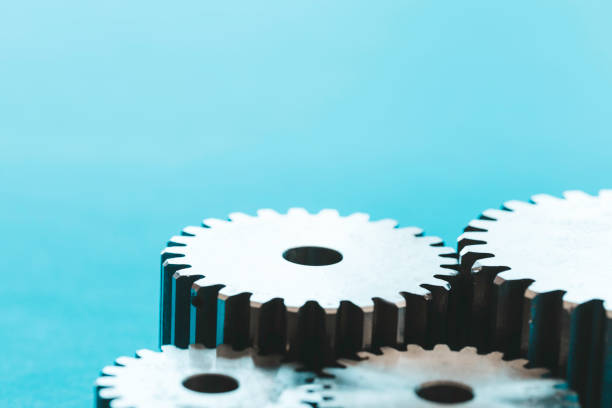 A close-up of interlocking gears against a blue background, symbolizing teamwork, cooperation, and efficiency. The gears convey the importance of connectivity and precision in machinery and engineering processes. Captured with no people in the frame, highlighting the mechanical focus.