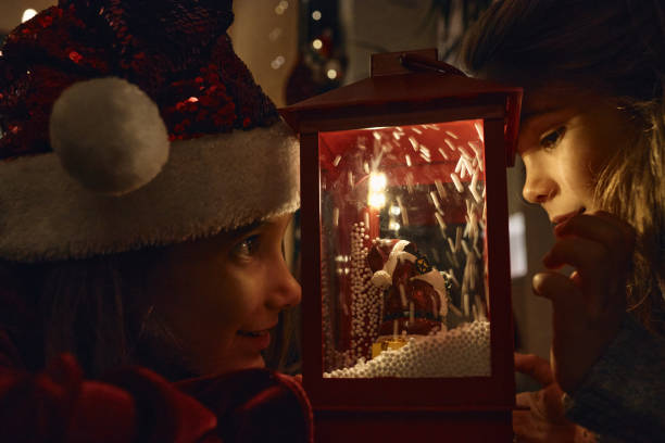 Beautiful girls on a New Year’s Eve looking at lantern with fake snow, dreaming about future.