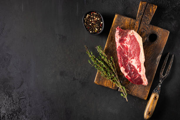 istock A raw beef steak rests on a rustic wooden cutting board with fresh thyme and a bowl of peppercorns, ready for cooking and seasoning 2185075924