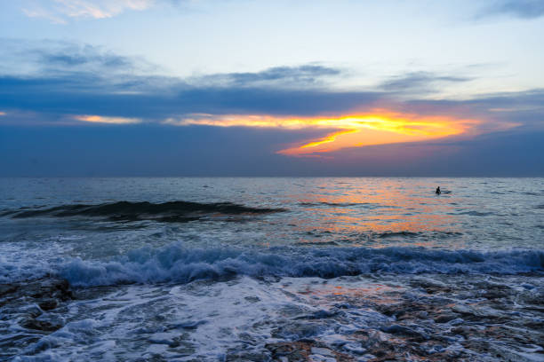 Serene seaside view of a sunset over the ocean, with waves gently lapping the shore and vibrant colors in the sky. Perfect for themes of tranquility and natural beauty.