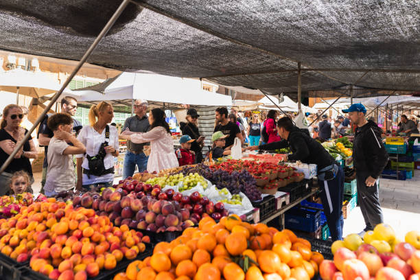 Santanyí, Spain -April 20, 2024: Two vendors stand at a vibrant fruit and vegetable stall in the famous Santanyí market, Mallorca. Surrounded by colorful produce and the hum of market life, they embody the authentic charm that draws locals and tourists year-round. Part of a series.