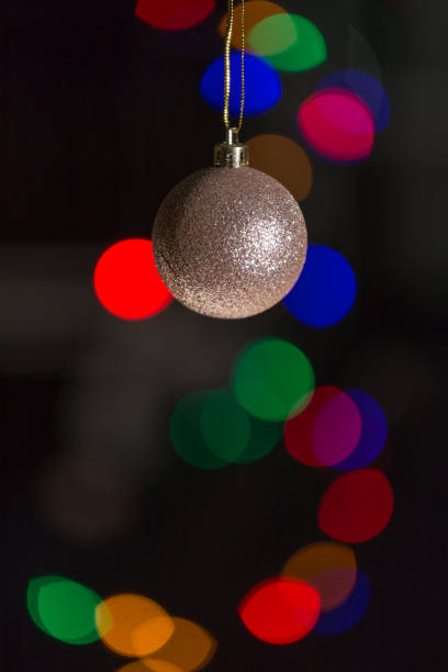 A golden Christmas ball hangs on a dark background, there are colored dots on one side, caused by out-of-focus lights