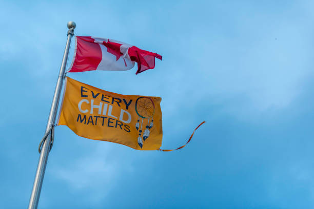 Toronto Ontario, Canada- November 1st, 2024: A Canadian flag and a Every Child Matter’s flag on a flag pole flapping in the wind.