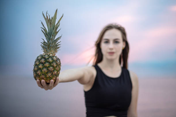 Young woman is holding pineapple on the outside at sunset.