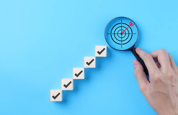 istock Goal Achievement Steps and Target Concept. Wooden blocks with checkmarks forming a staircase toward a magnifying glass highlighting a target, representing goal achievement and focus. business growth, 2185112724