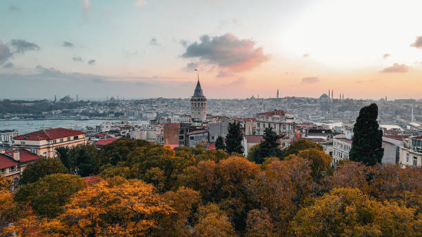 Drone photo moving from Istiklal Avenue to Galata Tower at sunset in Istanbul, Turkey, showcasing vibrant crowds, historic architecture, and scenic cityscape under warm evening light. drone footage of istanbul’s iconic istiklal avenue leading to galata tower at sunset, sunset drone journey over istiklal avenue to galata tower in istanbul, showcasing turkish cultural landmarks and the city’s blend of historical architecture