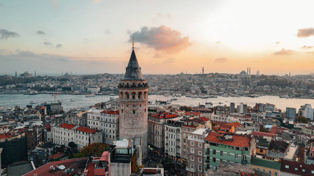 Drone photo moving from Istiklal Avenue to Galata Tower at sunset in Istanbul, Turkey, showcasing vibrant crowds, historic architecture, and scenic cityscape under warm evening light. drone footage of istanbul’s iconic istiklal avenue leading to galata tower at sunset, sunset drone journey over istiklal avenue to galata tower in istanbul, showcasing turkish cultural landmarks and the city’s blend of historical architecture