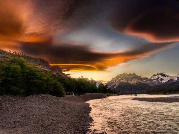 Golden clouds stretch over Patagonias rugged mountains and flowing river, creating a dramatic and serene sunset scene, capturing natures raw beauty and peaceful atmosphere