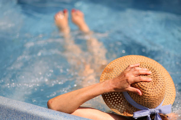 woman with hand on straw hat on head sitting inside the tub with massaging and relaxing bubbles during luxury cruise