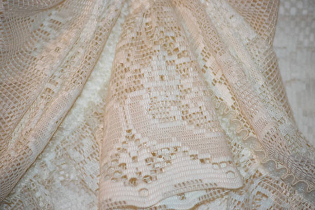 Detailed image of an intricate white lace fabric showcasing elegant patterns and textures. The delicate design highlights craftsmanship, adding a touch of elegance and vintage charm.