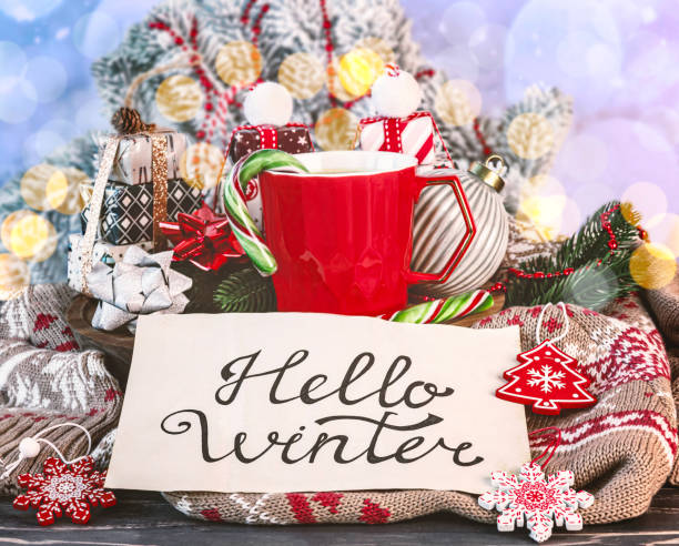 istock Lettering on paper hello winter, beige cup of coffee, Christmas decorations, gift boxes, lollipops, warm sweater, fir branches 2185127748