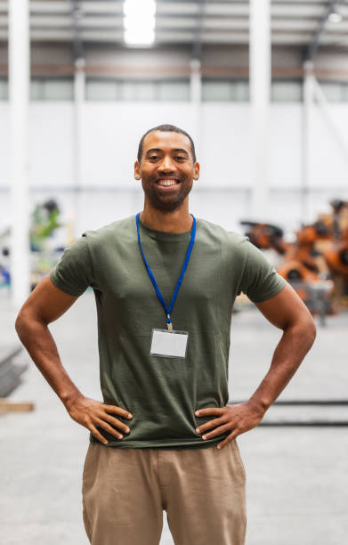 istock Smiling black engineer posing with hands on hips in factory 2185128171