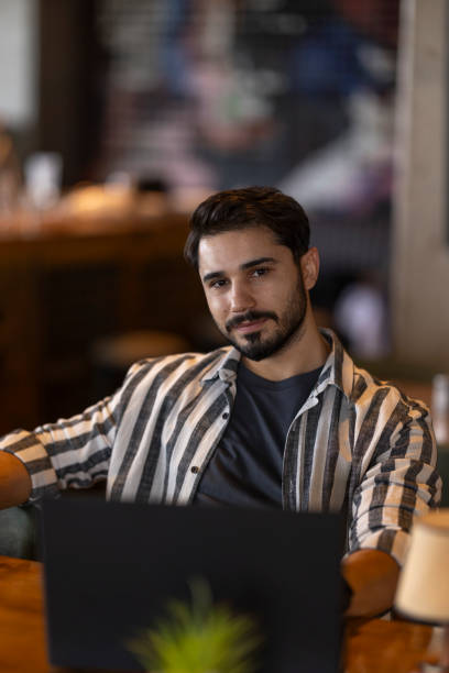 istock Young businessman working on laptop in a cafe, looking at camera 2185130812