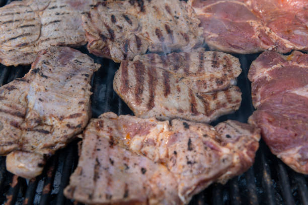 Detailed view of pork steaks cooking on a grill, with charred lines and smoky essence, perfect for barbecue and food-related themes.