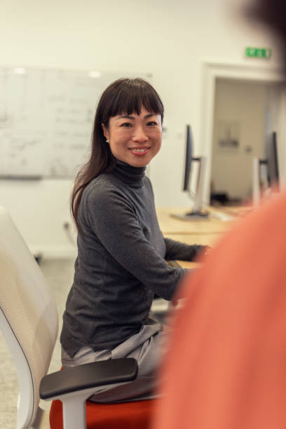 istock Smiling female Japanese software engineer looking directly at camera while sitting at desk in work environment 2185134135