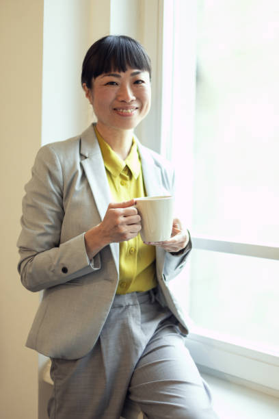 Smiling Asian business woman drinking coffee while standing in the office