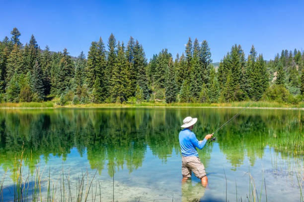 Eagle County Emerald Lake with coniferous trees and mirror sky reflection on water surface and man fishing with rod and reel