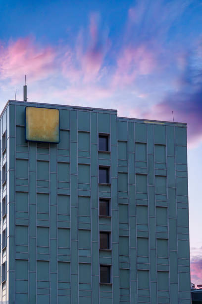 A modern office building with a geometric design is captured during twilight. The structure features large windows and a contemporary exterior, with no people visible in the urban scene