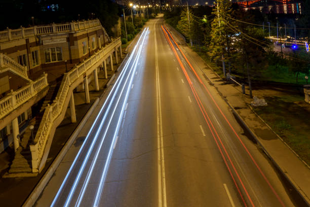A city street at night with light trails from passing vehicles captured in long exposure. The road is empty with no people, creating a sense of calm and motion in the urban evening scene