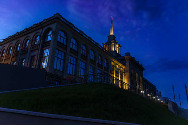 A historic building with large windows is illuminated at dusk, showcasing classical architectural design. The evening light reflects off the windows