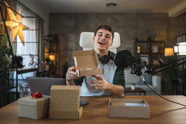 istock Young adult man open gifts while streaming with microphone and laptop 2185158443