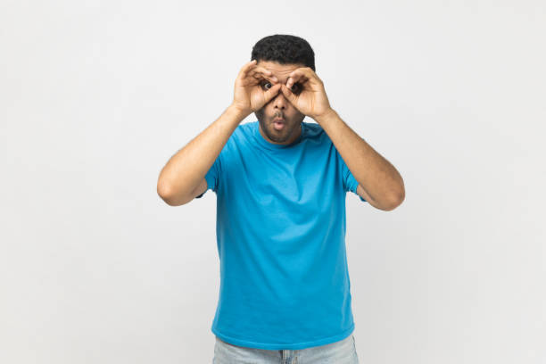istock Man making glasses shape with fingers, looking through binoculars hand gesture and expressing shock. 2185161503