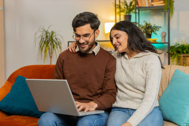 istock Happy young diverse couple family discussing planning together booking while using laptop at home 2185164175