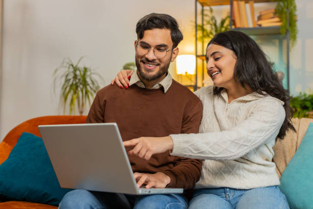 istock Happy young diverse couple family discussing planning together booking while using laptop at home 2185164183