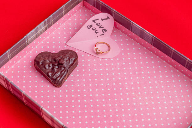 Wedding ring with diamond chocolate and pink heart in pink box on red background High quality photo.