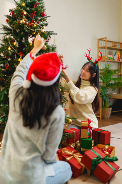 istock Two friends happily decorating a Christmas tree with ornaments, surrounded by gift boxes. The holiday spirit is enhanced by a festive, glittering backdrop. 2185186164
