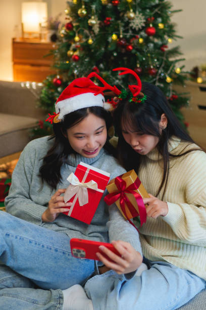 istock Two friends wearing festive headbands, sitting by the Christmas tree, joyfully video calling with loved ones during the holiday season 2185186205