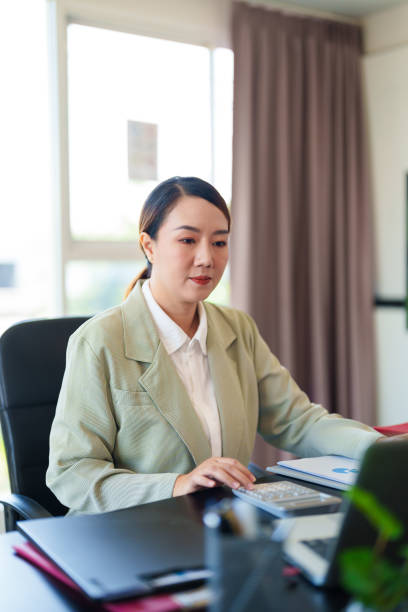istock A professional woman in a light suit sits at a desk, focused on her work with documents and a laptop in front of her. The bright office setting 2185188253