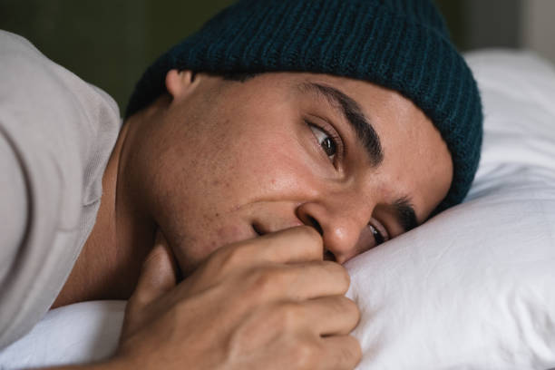 istock Young man feeling sad lying in bed wearing a beanie 2185190895