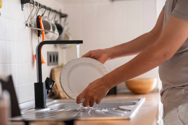 istock Man washing dishes in kitchen sink with tap water running 2185191019