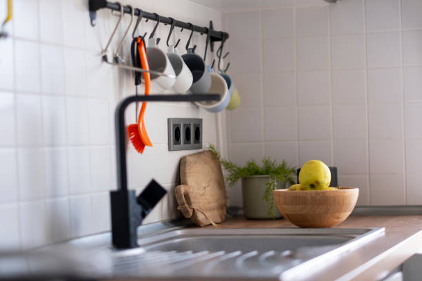 Close-up view of a contemporary kitchen design showcasing hanging cups, a wooden cutting board, a bowl of apples, and a sleek black faucet