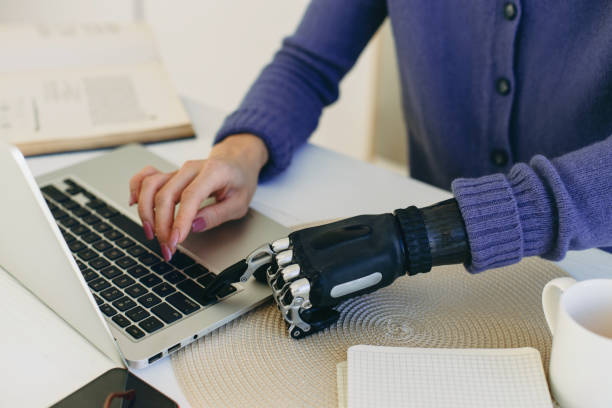 istock Crop shot of female typing on keyboard in artificial bionic arm prosthesis, dressed in veri peri cardigan, sitting at table desk working online, studying, sending e-mail. Biomedical engineering 2185193410