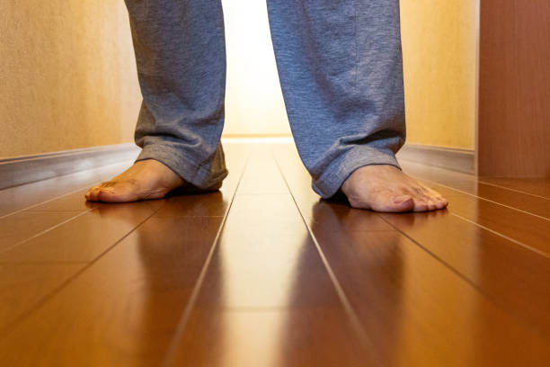 Close-up image of a person wearing stylish black leather dress shoes and gray trousers. The background features a vibrant yellow fabric, creating a striking contrast with the formal footwear. The image highlights the elegant design and polished finish of the shoes, suitable for business or formal settings