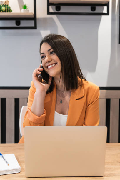 istock Smiling female freelancer sitting at table with laptop and using a phone 2185196959