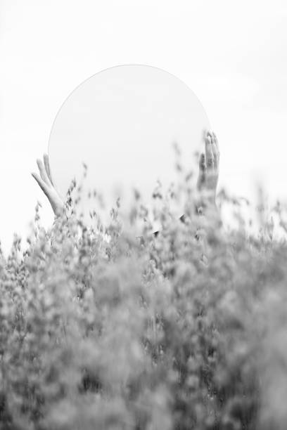 Nature concept, states of mind and mystery concept. Woman hands holding a mirror among wheat, reflecting the sky. Image contains noise and motion blur. Black and white image