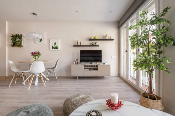 istock Spacious living room with large windows, dining table on the backdrop of a wall with a TV, shelves and decorative accessories and plants. Concept of functional and stylish apartment interior 2185200277
