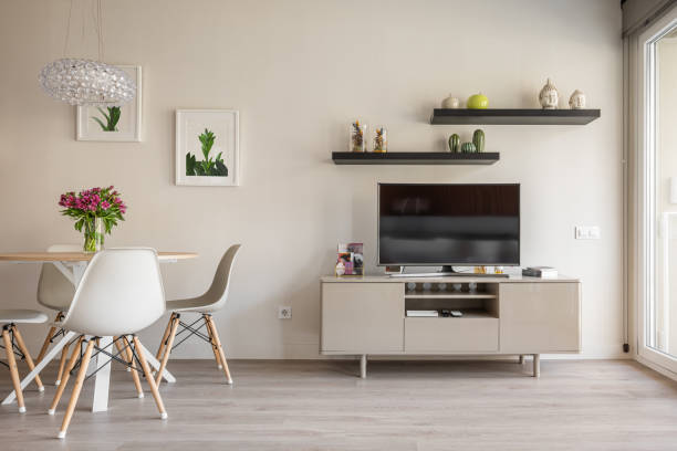 istock Cozy living room with panoramic windows, a dining table and chairs against the backdrop of a wall with a TV, shelves and decorative accessories and flowers. Concept of a stylish apartment interior 2185200283
