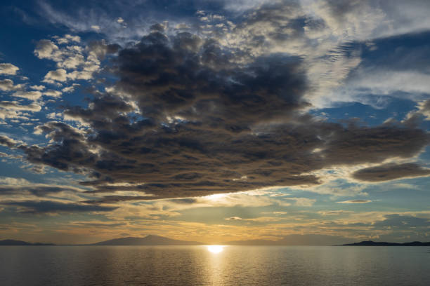 This image captures a breathtaking sunset over Aegean sea in Greece, with dramatic clouds casting intricate shadows and colours, conveying a sense of tranquillity and awe.