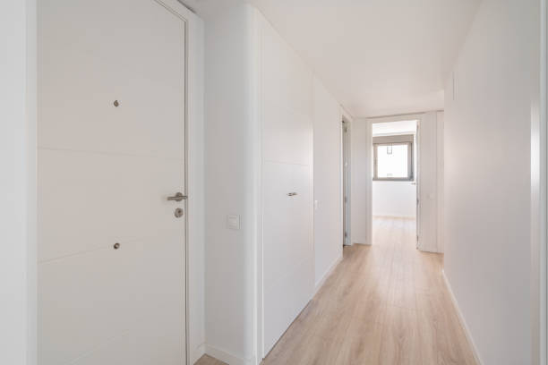Narrow white corridor with doors and entrances to different rooms and premises and resting on a room with a window on the sunny side. Concept of minimalist design in a new apartment