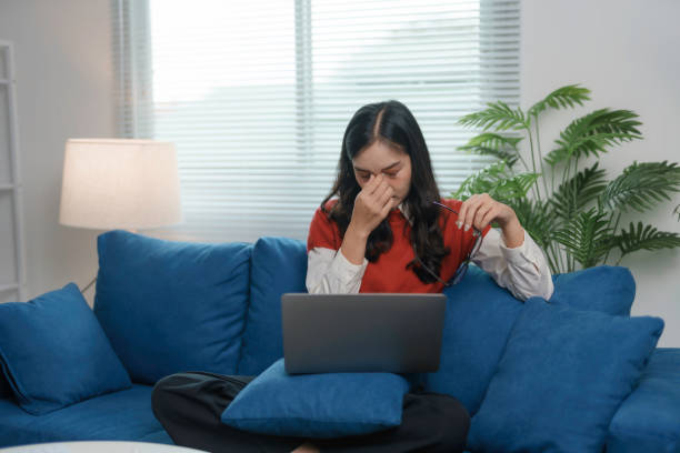 istock Tired young woman takes a break from working on her laptop while sitting on a blue sofa, removing her glasses and rubbing her eyes 2185207886