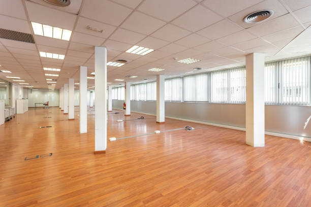 istock Empty office and fluorescent lamps on the ceiling in need of repair and replacement. Bright office space for rent. Light brown parquet and large panoramic windows in an empty abandoned office. 2185209640