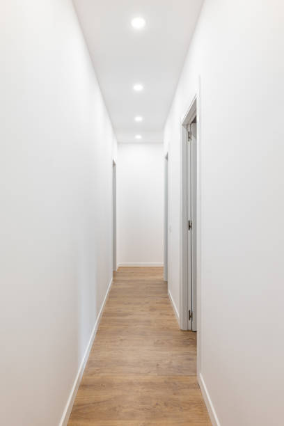 istock Long corridor with white smooth walls, bright light pours from spotlights from the ceiling, wooden laminate flooring, open doors on both sides to separate living rooms. 2185209952