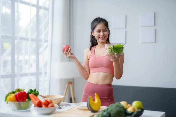 istock Young woman is smiling while comparing a salad and an apple, surrounded by fresh produce in her kitchen 2185209958