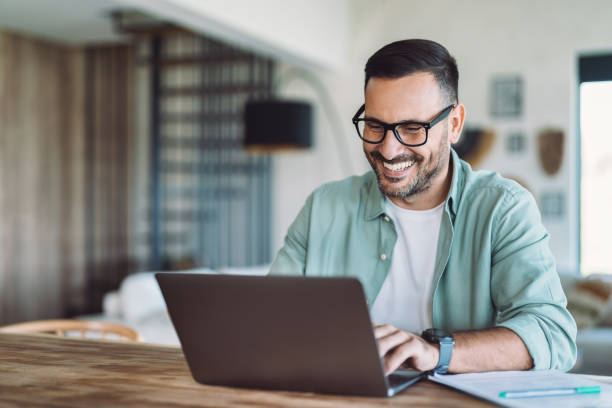 istock Smiling businessman using laptop in his living room 2185212336