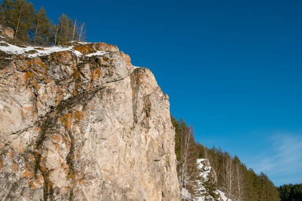 A rocky mountain with snow on it and a clear blue sky. The sky is very bright and the snow is white